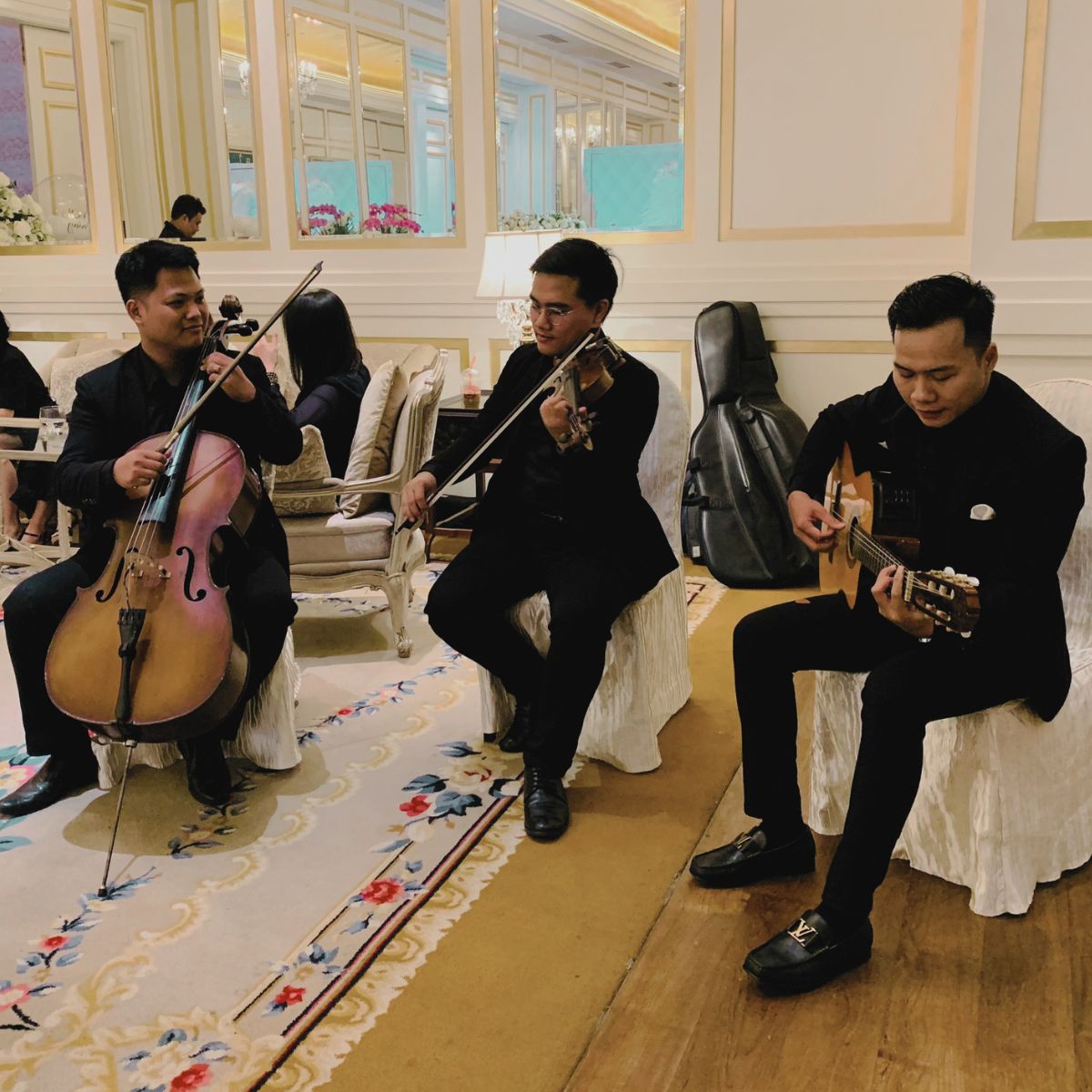 Bộ ba cello, violin và guitar chuẩn bị biểu diễn trong không gian tiệc cưới.